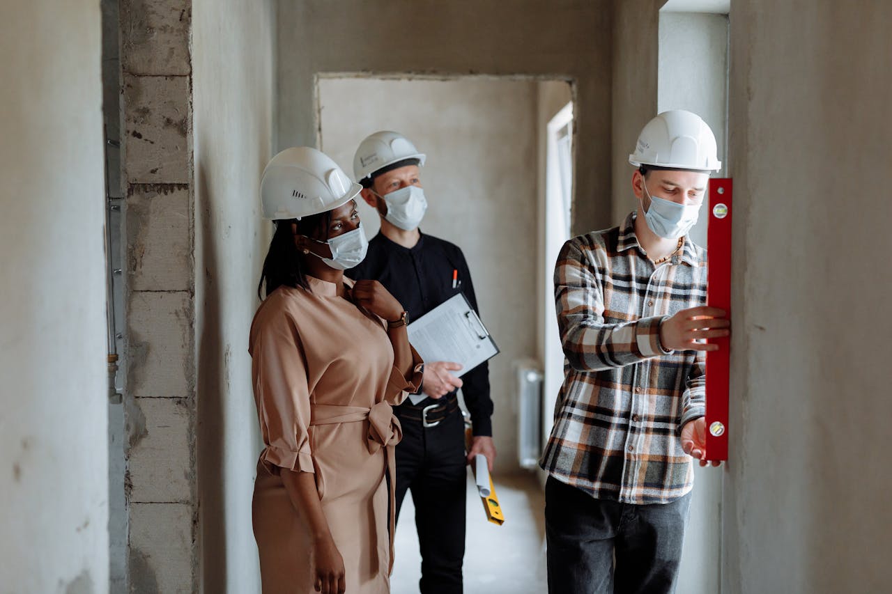 Three professionals wearing safety gear and face masks inspecting an unfinished building.