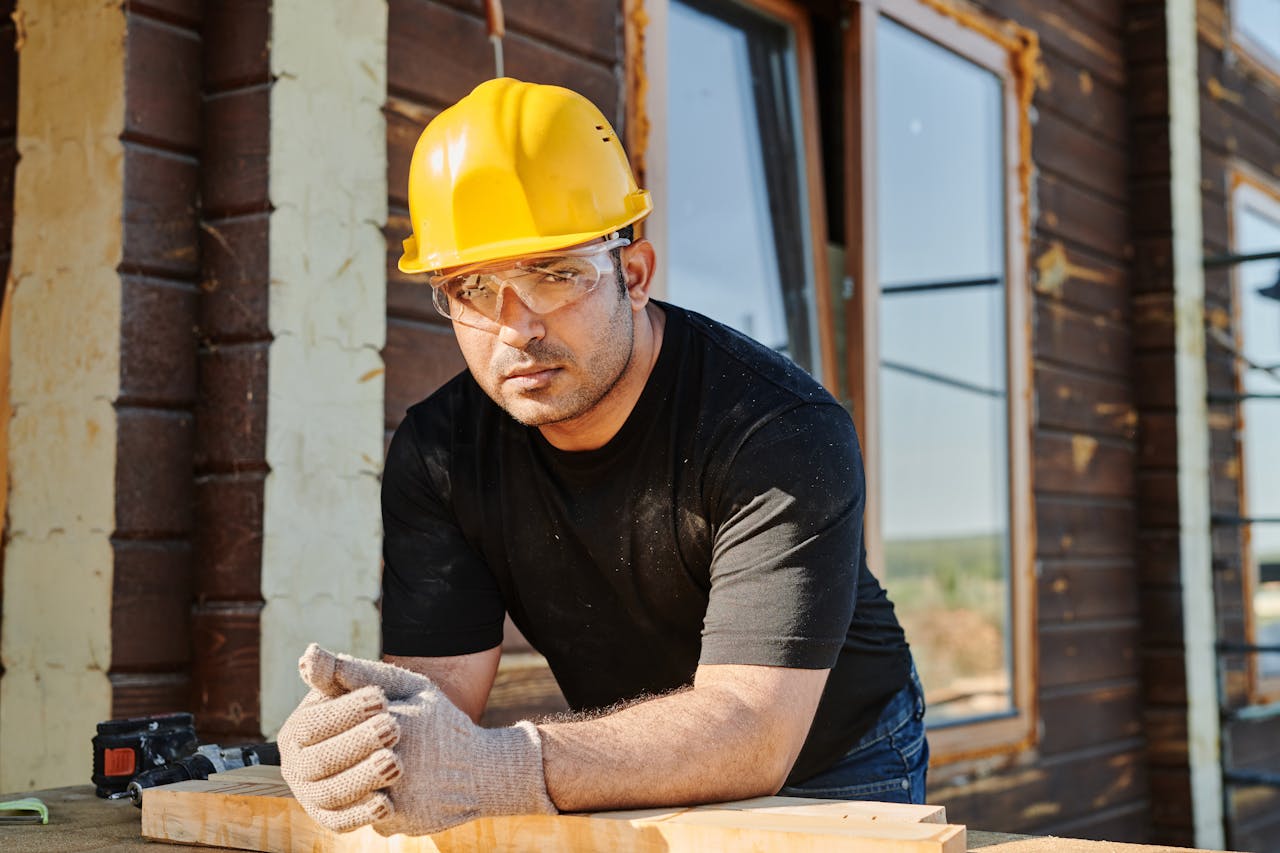 Focused construction worker with safety gear at a woodwork site.